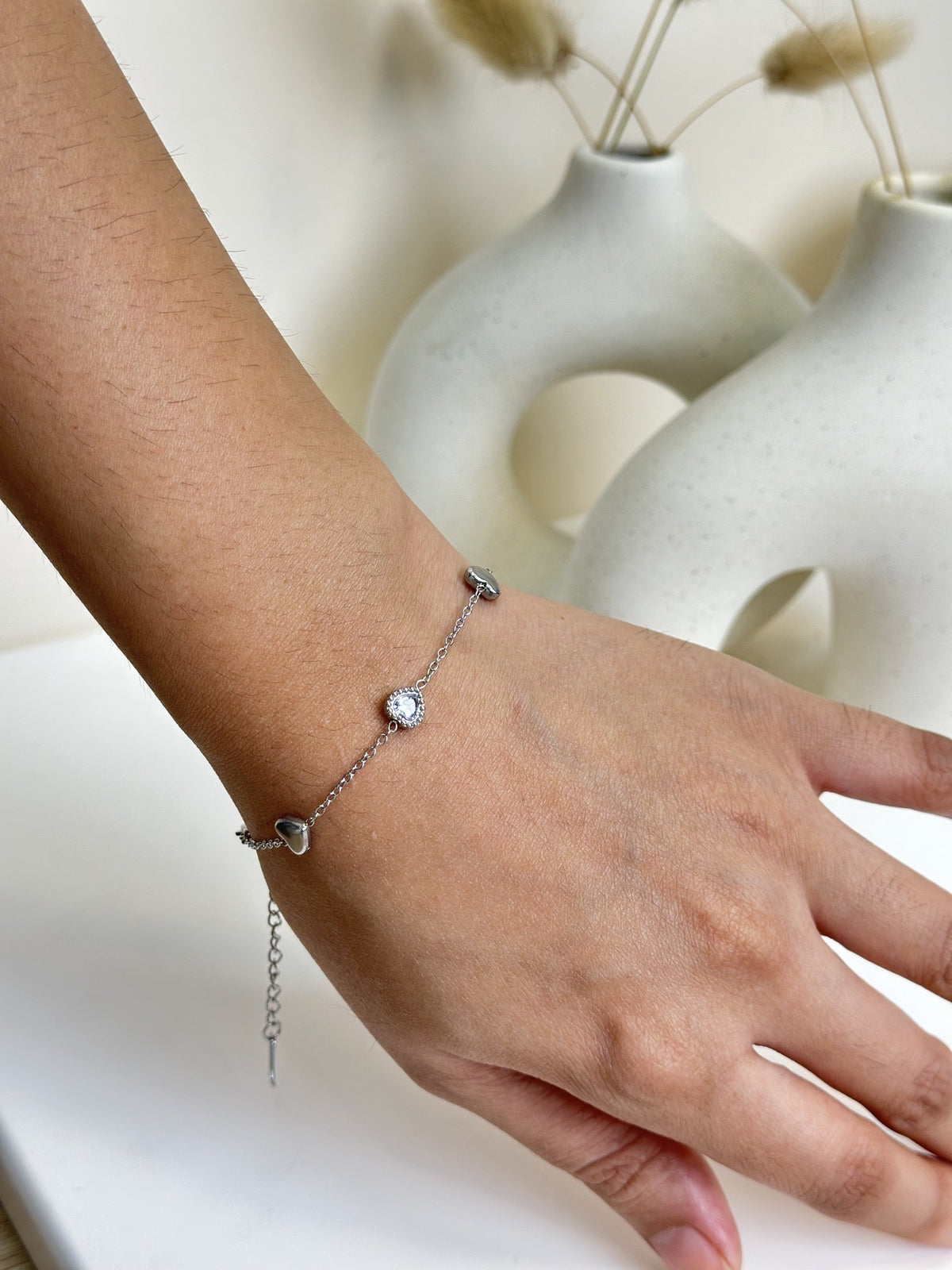 Paired Arlisse Bracelet in silver-tone, worn on the hand with heart charms, a clear stone and extension chain