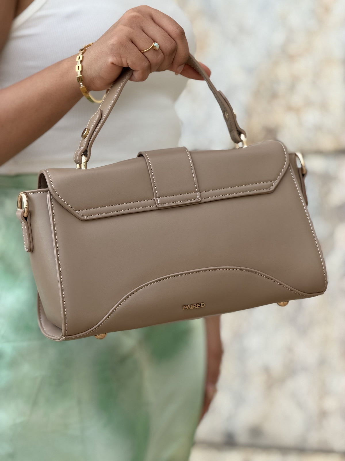 Paired Aurea Crest Bag in taupe apricot, held by the top handle, seen from the back with a stitched flap