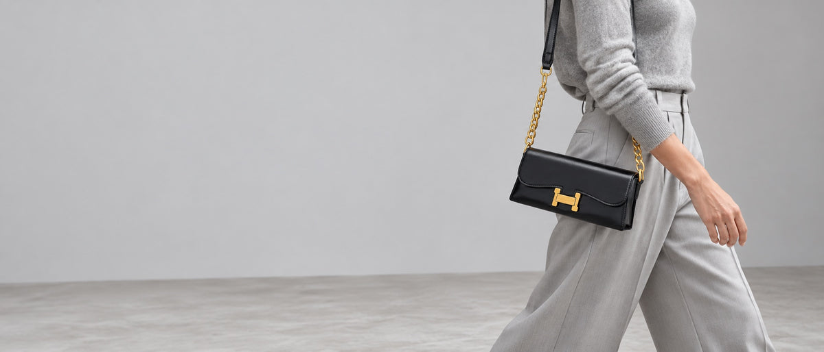 Woman in grey knitwear carrying the black Paired H-Buckle shoulder bag with gold chain strap
