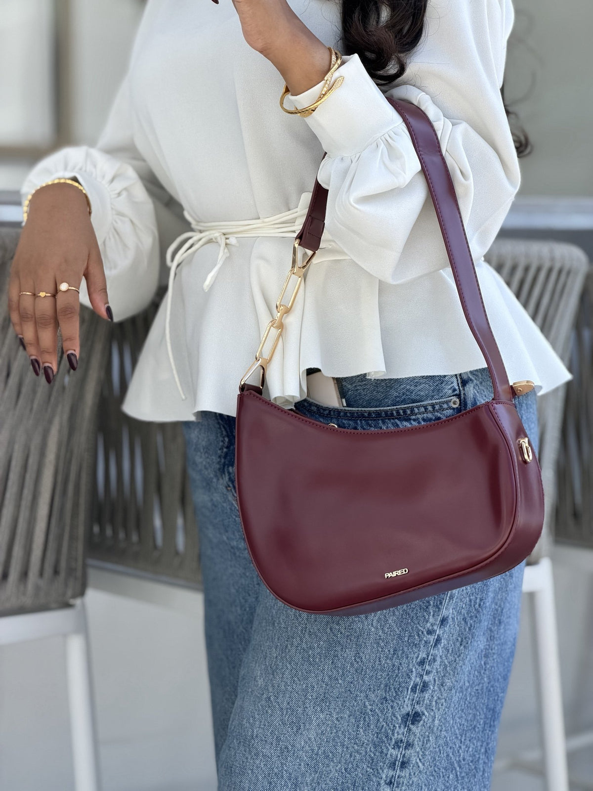 Paired Clarissa Chain Bag in burgundy, worn on the shoulder with a flat strap, with a white blouse and wide-leg jeans