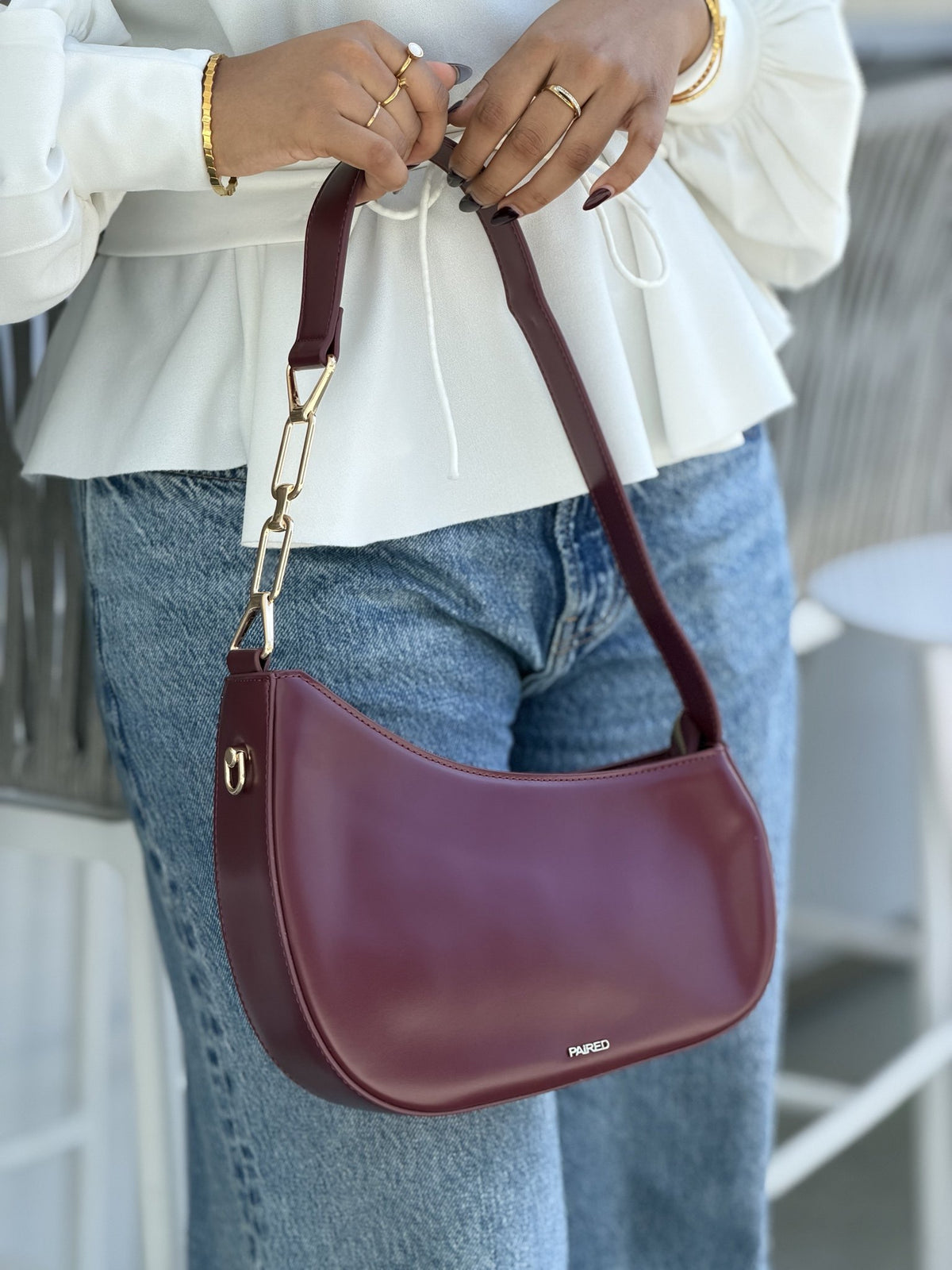Paired Clarissa Chain Bag in burgundy, worn on the shoulder with a flat strap and gold-tone chain link, white blouse