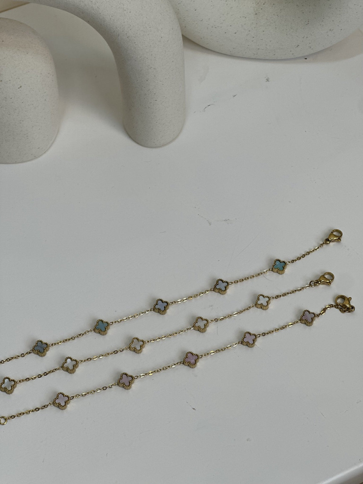 Paired Clover Petite Bracelet in gold-tone, three bracelets laid flat with clasps and pastel clover motifs