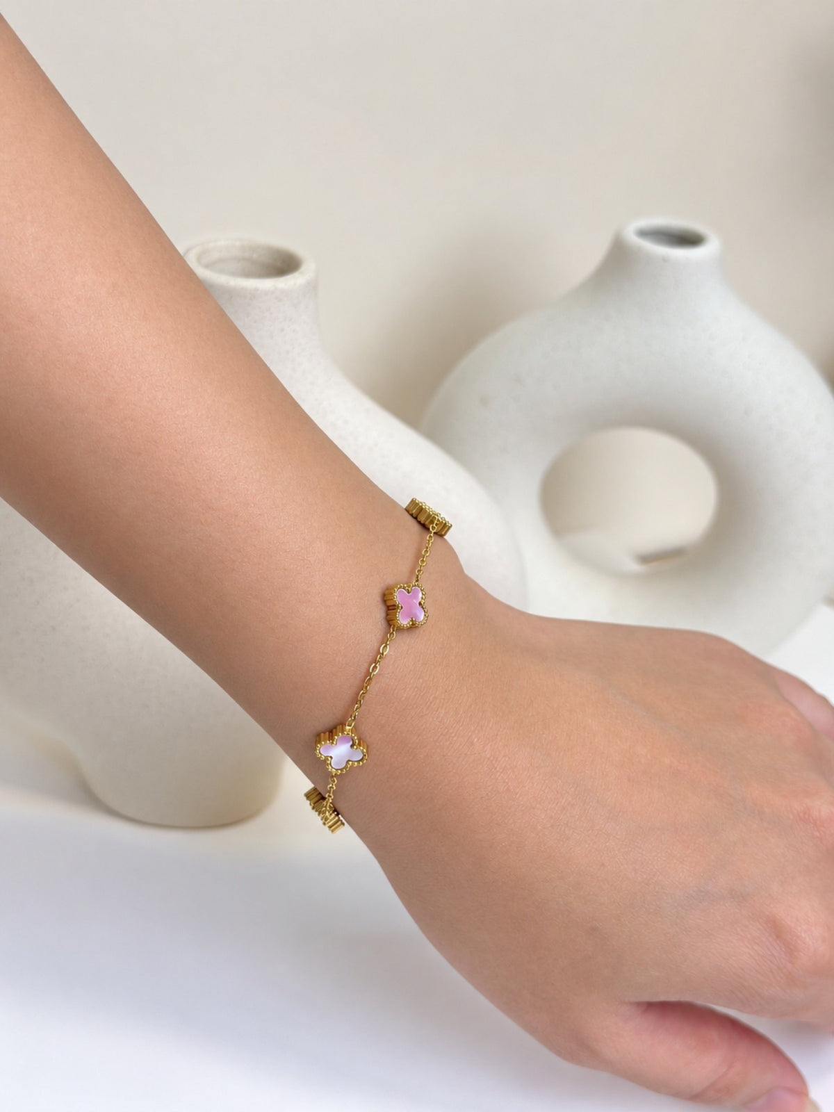 Paired Clover Signature Bracelet in gold-tone, worn on the wrist with pink and white clover-shaped motifs
