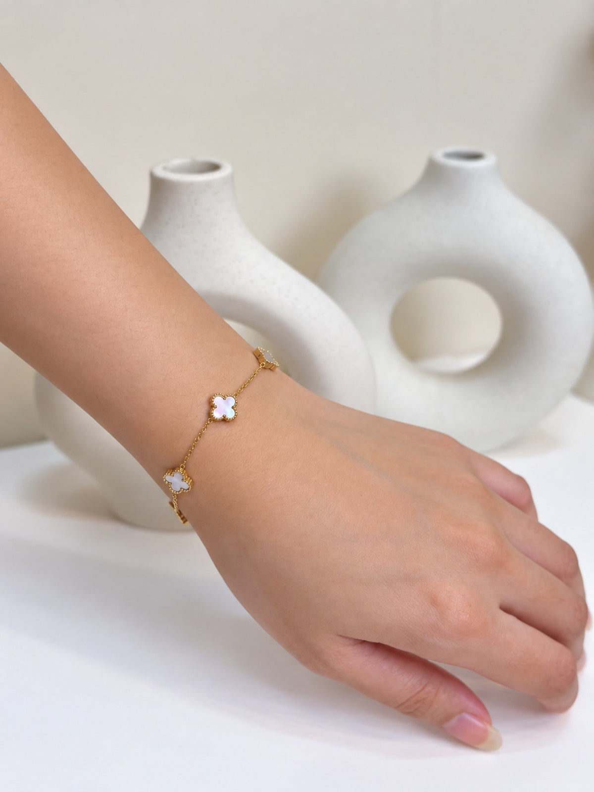 Paired Clover Signature Bracelet in white, gold-tone chain worn on the hand with clover-shaped motifs