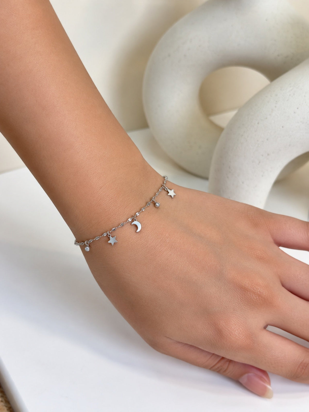 Paired Cressida Bracelet in silver-tone, worn on the wrist with a delicate chain and dangling star and moon charms