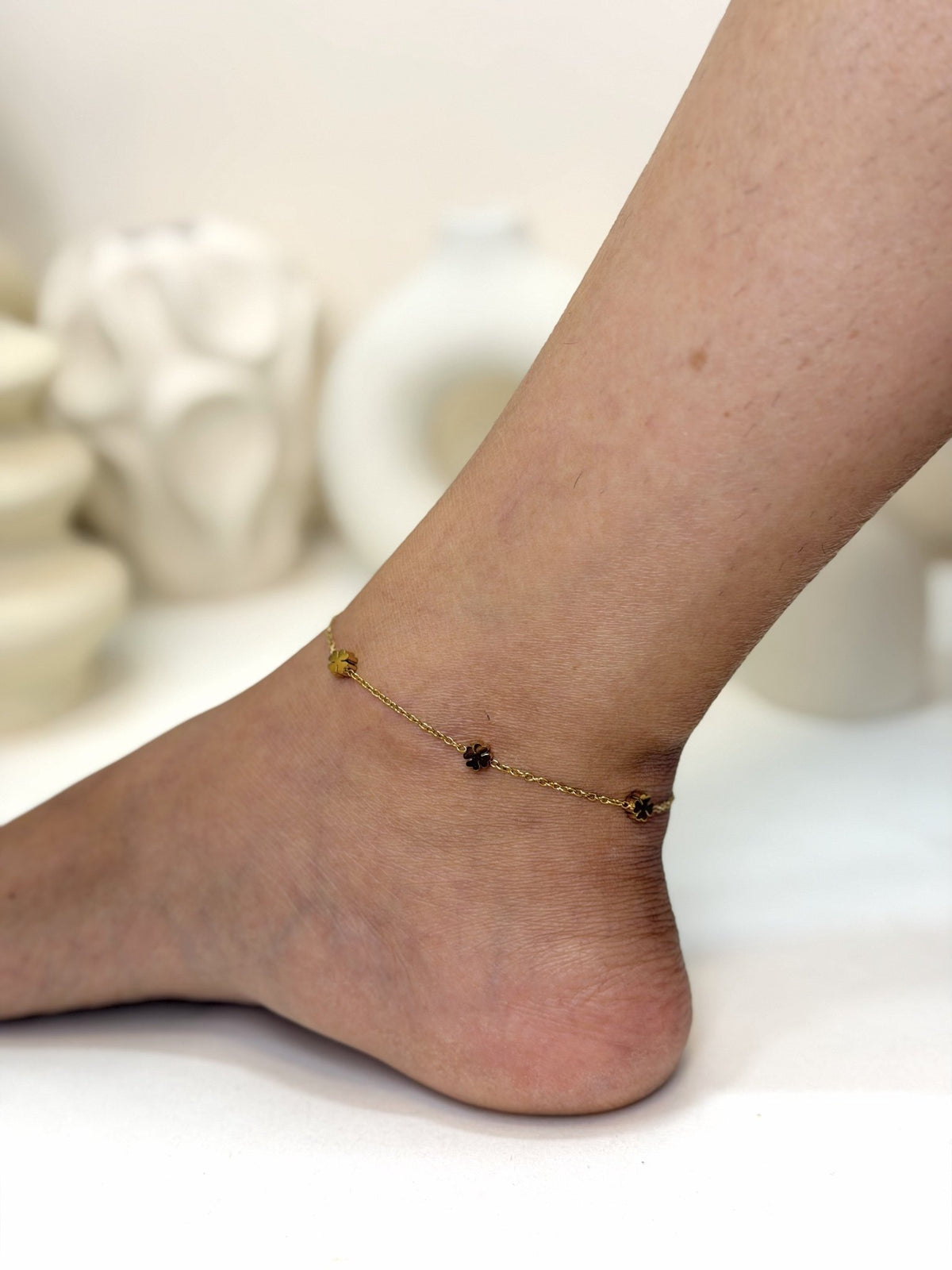 Paired Elara Anklet in gold-tone, worn on the ankle showing flower-shaped charms along a fine chain