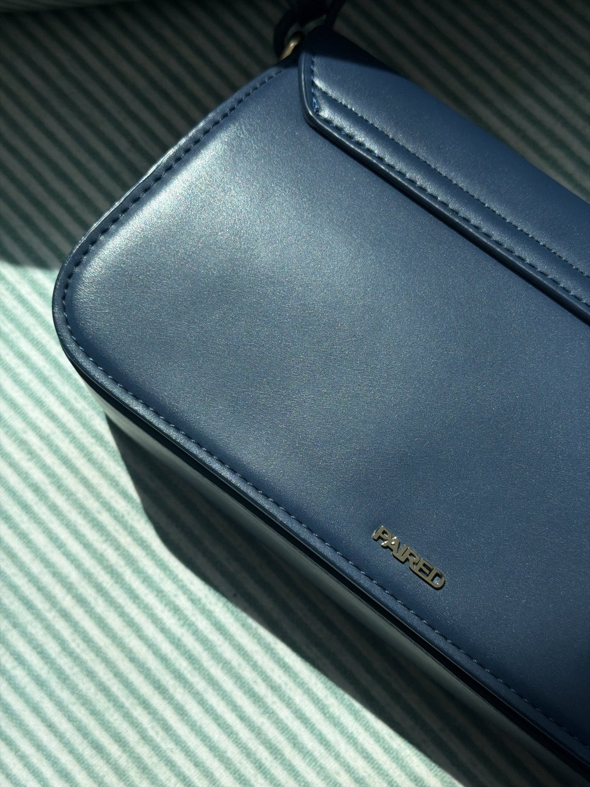 Paired Elise Lock Bag in navy blue, close-up of the smooth navy blue corner with the Paired logo on a striped cloth