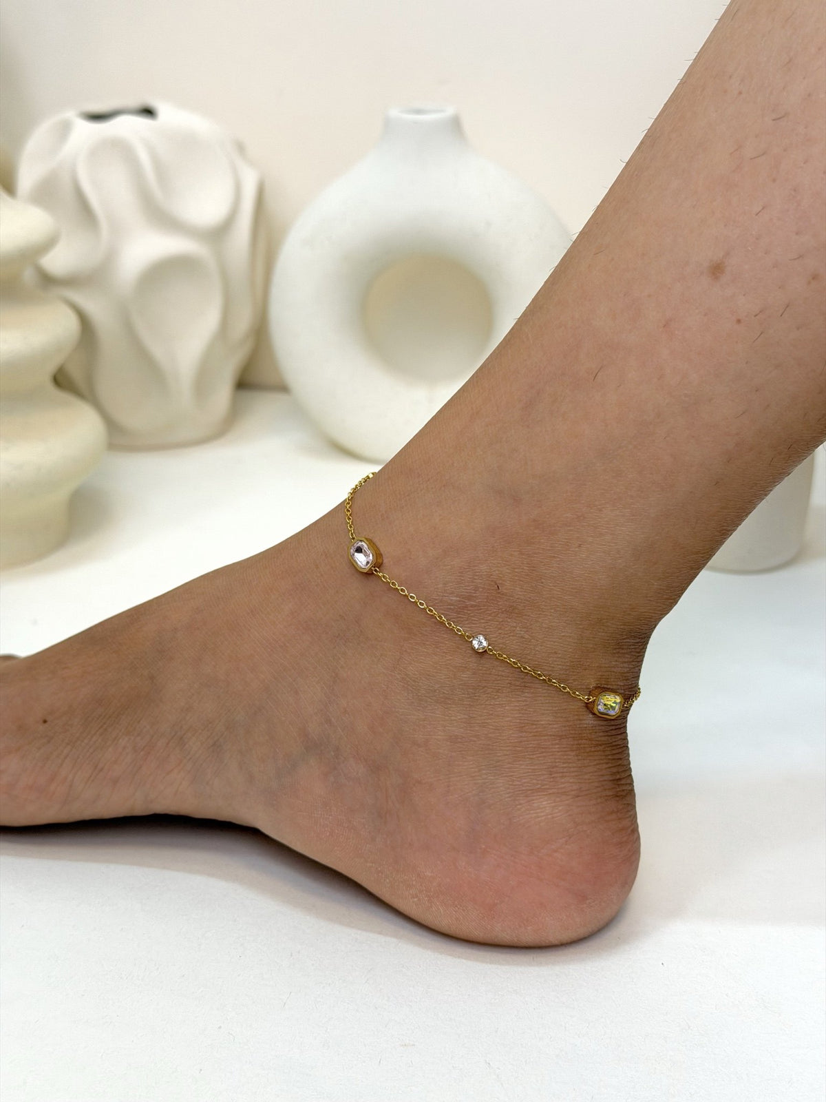 Paired Evania Anklet in gold-tone, side view on the ankle with rectangular stones and small clear accents