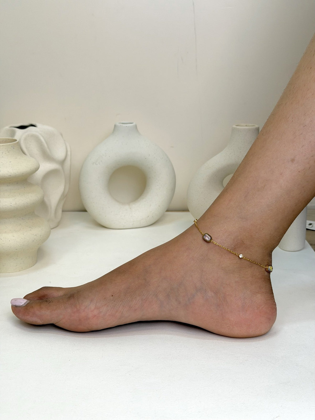 Paired Evania Anklet in gold-tone, worn on the foot and ankle with soft-toned stones on a fine chain