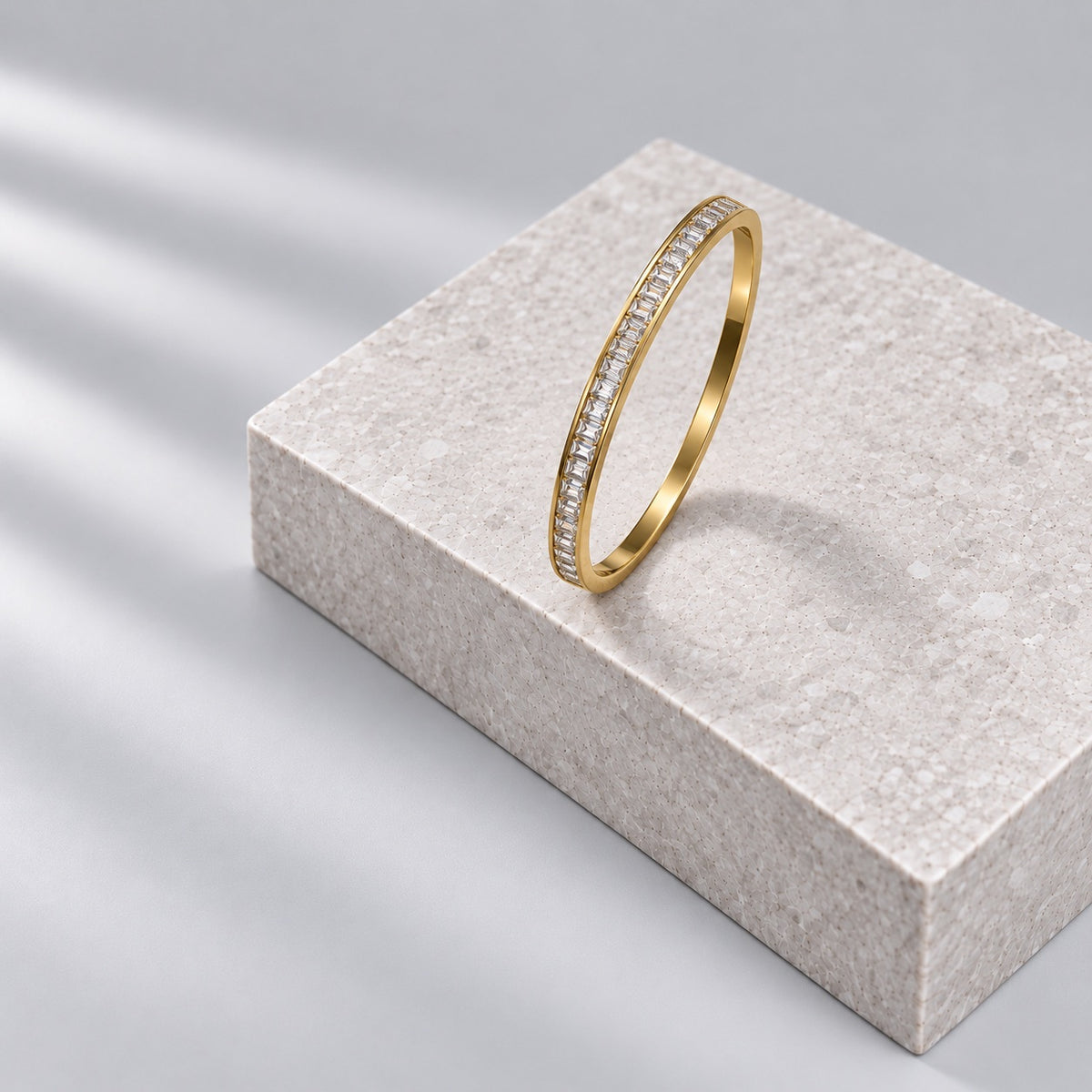 Paired gold bangle with a row of crystals on a grey stone plinth