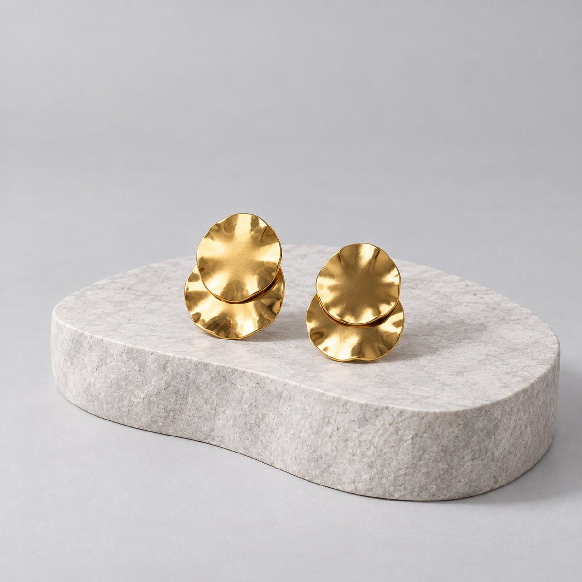 Paired gold wave earrings on grey stone