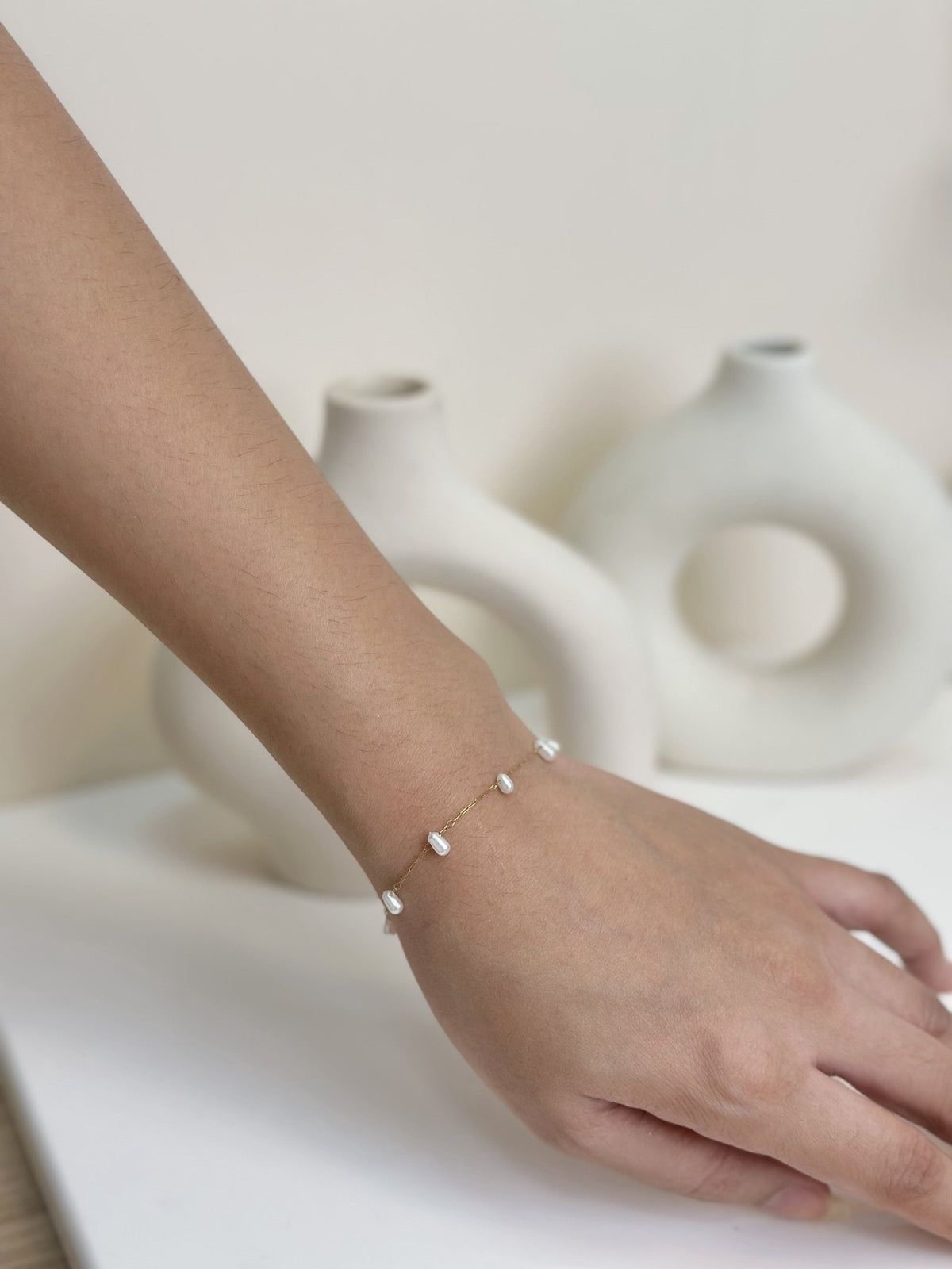 Paired Laurentia Bracelet in gold-tone, side view on the wrist with white oval beads on a very fine chain