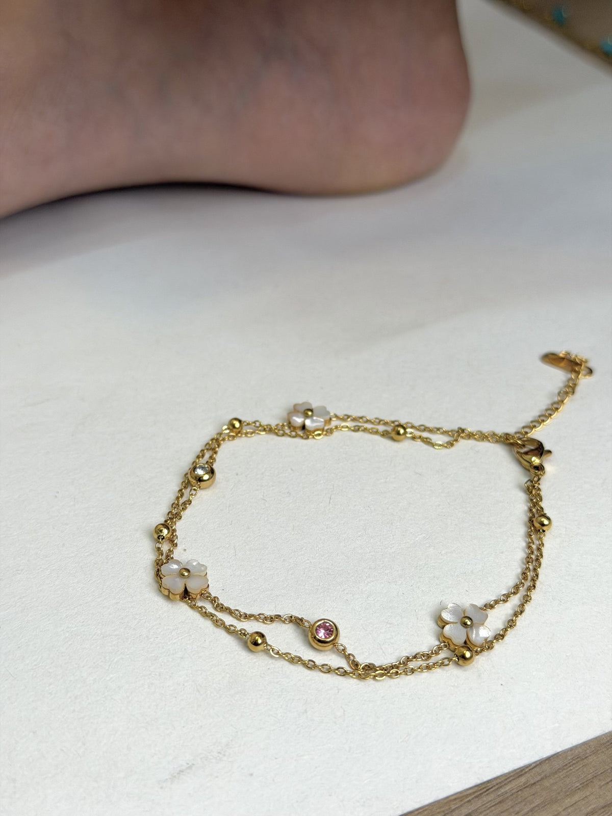 Paired Liora Anklet in gold-tone, laid flat showing double chains, white clover charms, beads and a pink stone