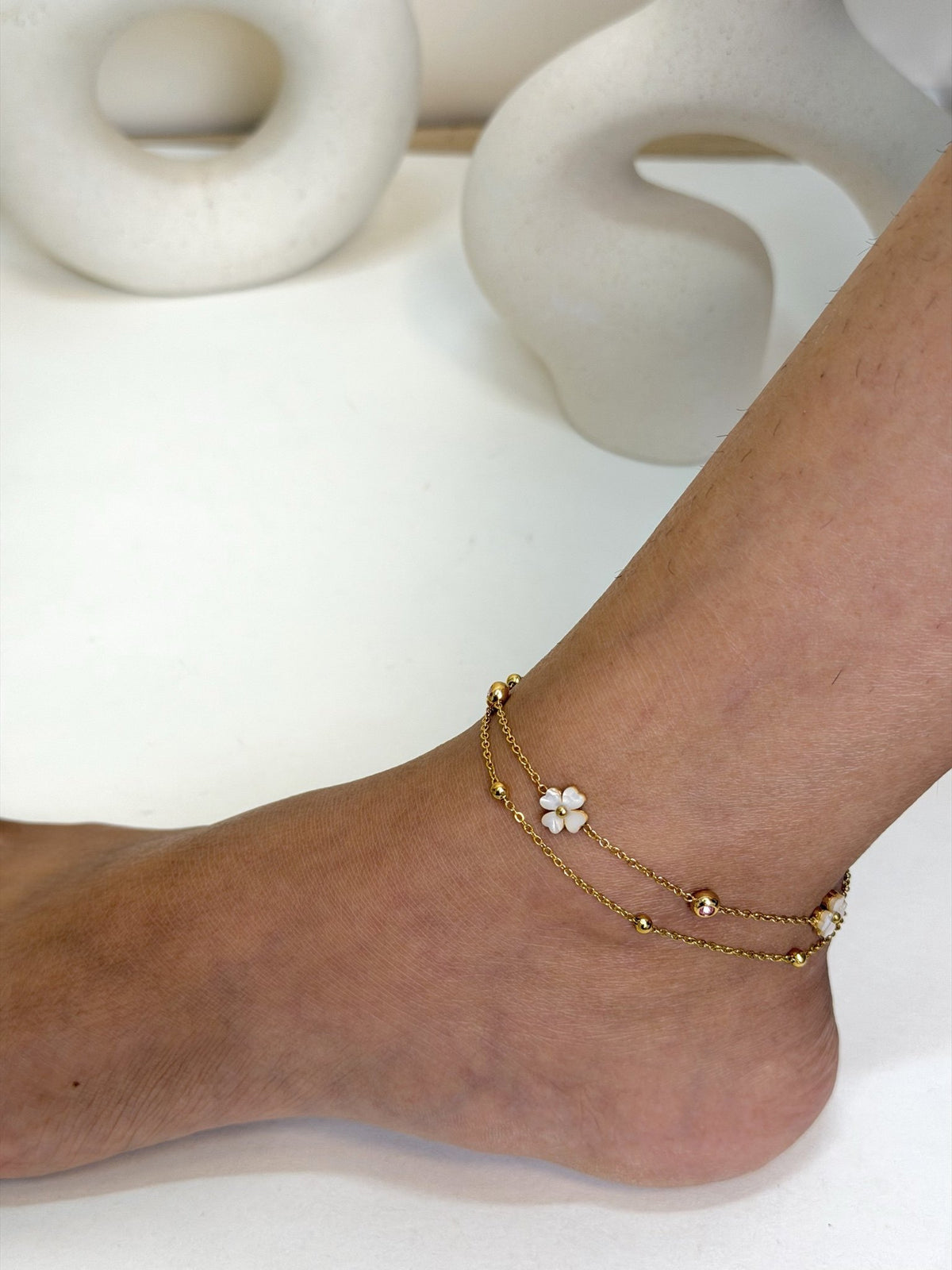 Paired Liora Anklet in gold-tone, three-quarter view on the ankle with double chains and a white clover charm