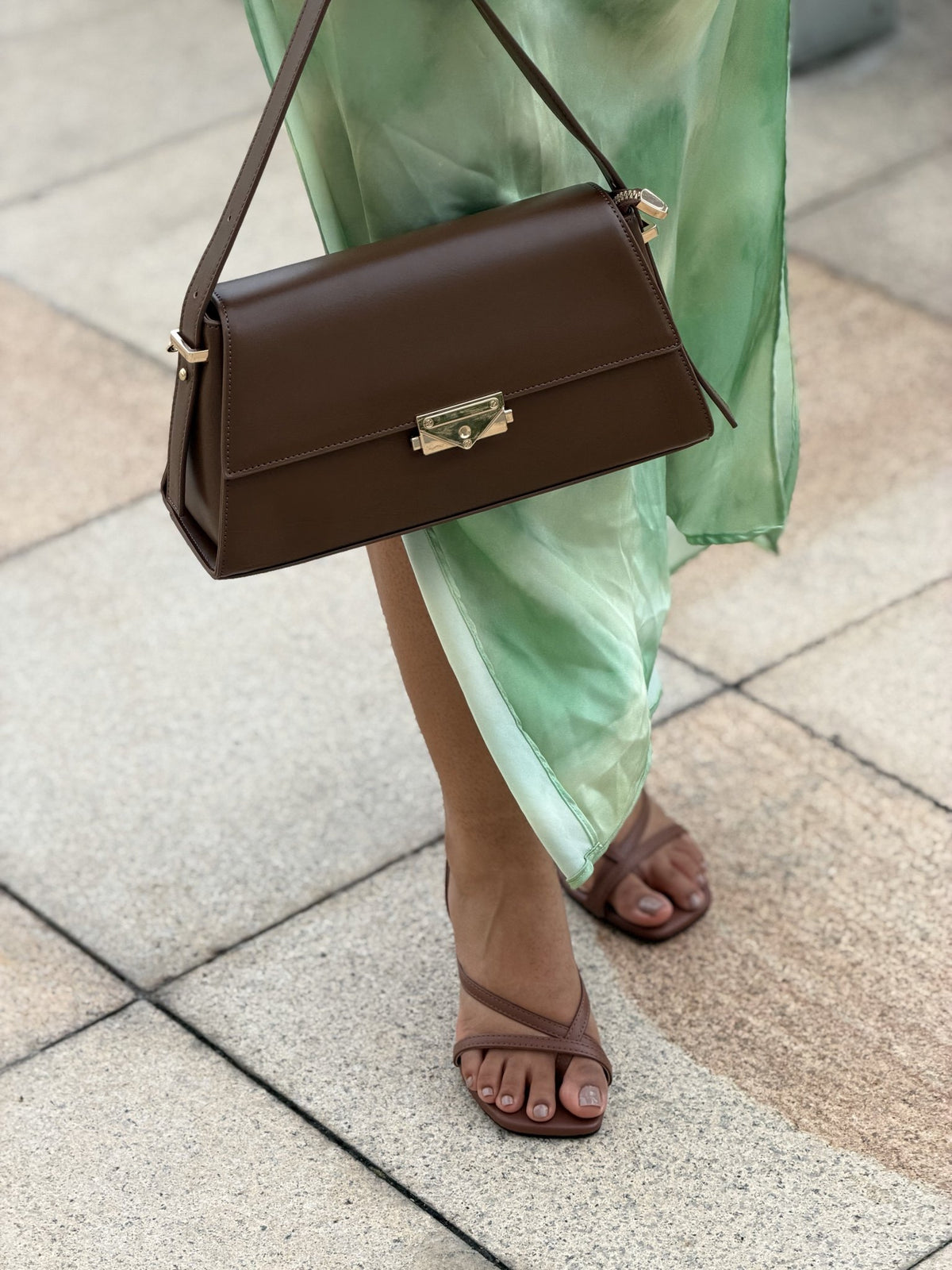 Paired Liora Frame Bag in coffee brown, worn on the shoulder by a slim strap with a green satin skirt and sandals