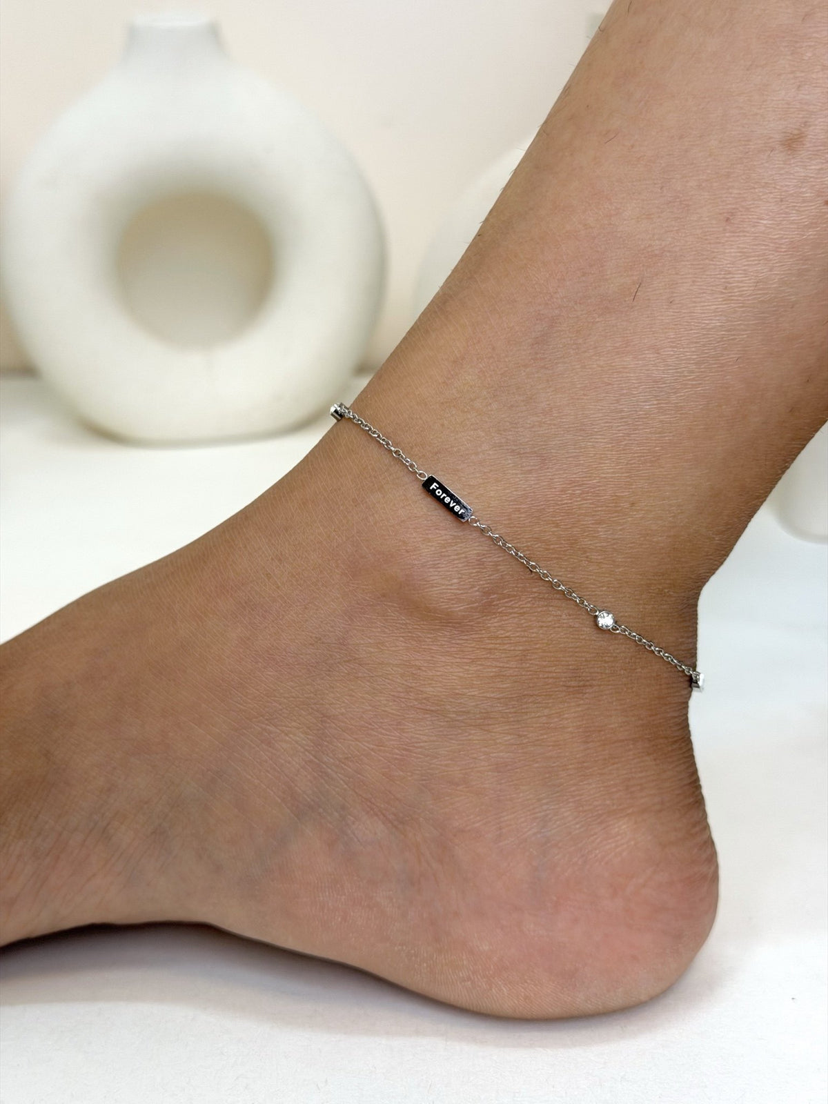 Paired Marielle Anklet in silver-tone, worn on the ankle showing the slim black bar and small clear stone