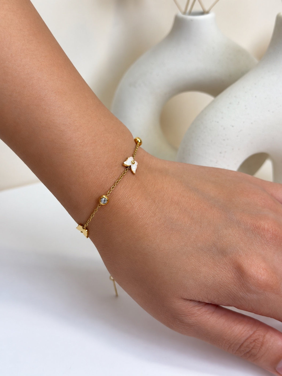 Paired Nerisse Bracelet in gold-tone, worn on the wrist with a white butterfly charm, small beads and an adjustable tail