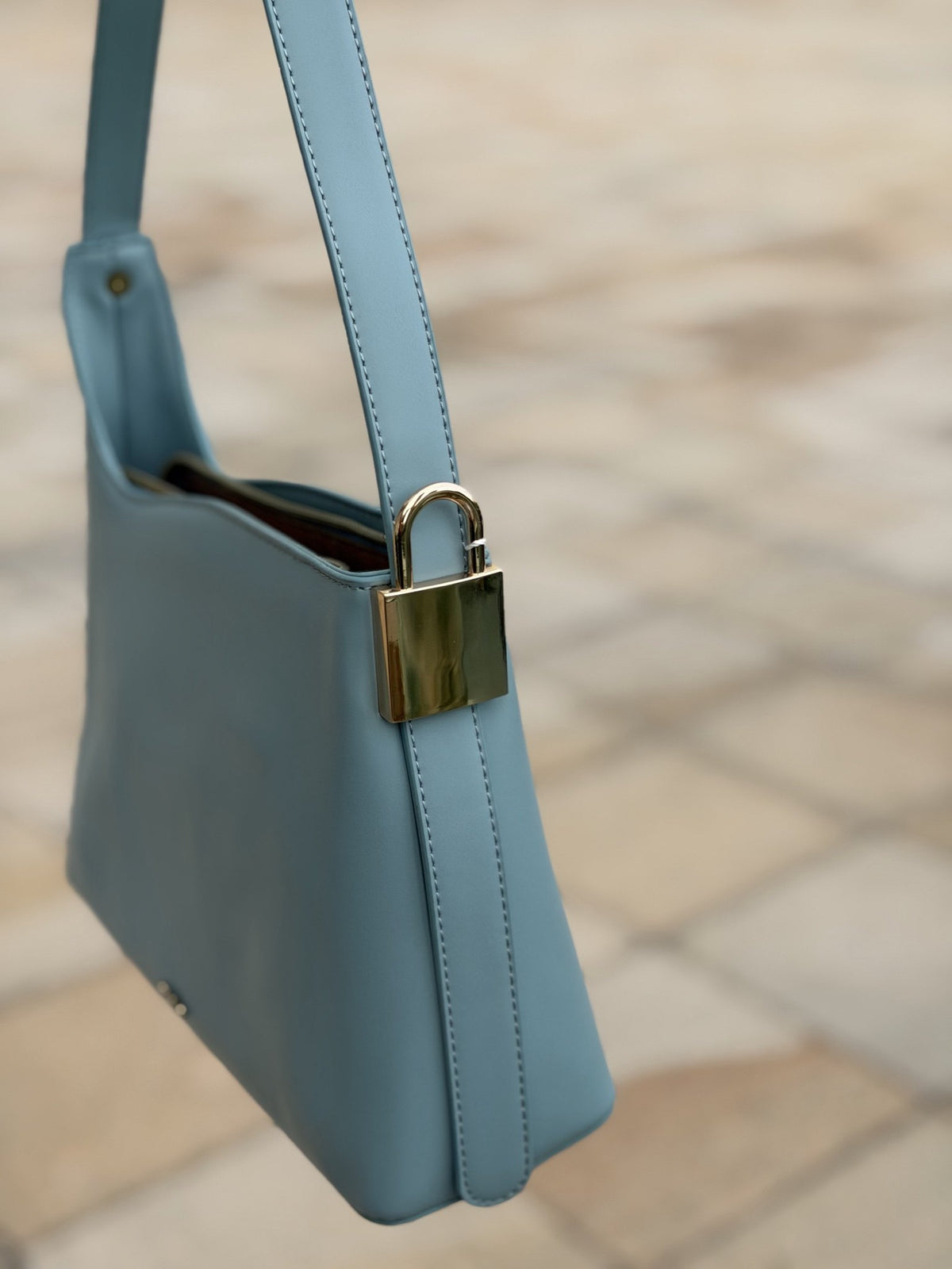 Paired Oriana Gold-Lock Bag in soft blue, hanging from its strap with a gold-tone padlock charm on the side
