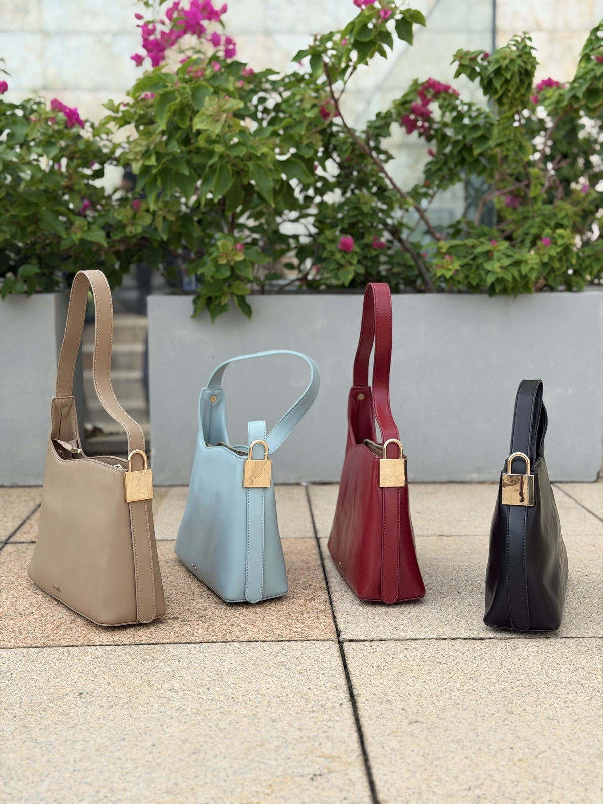 Paired Oriana Gold-Lock Bag in taupe, blue, red and black, standing in a row, each with a gold-tone padlock charm