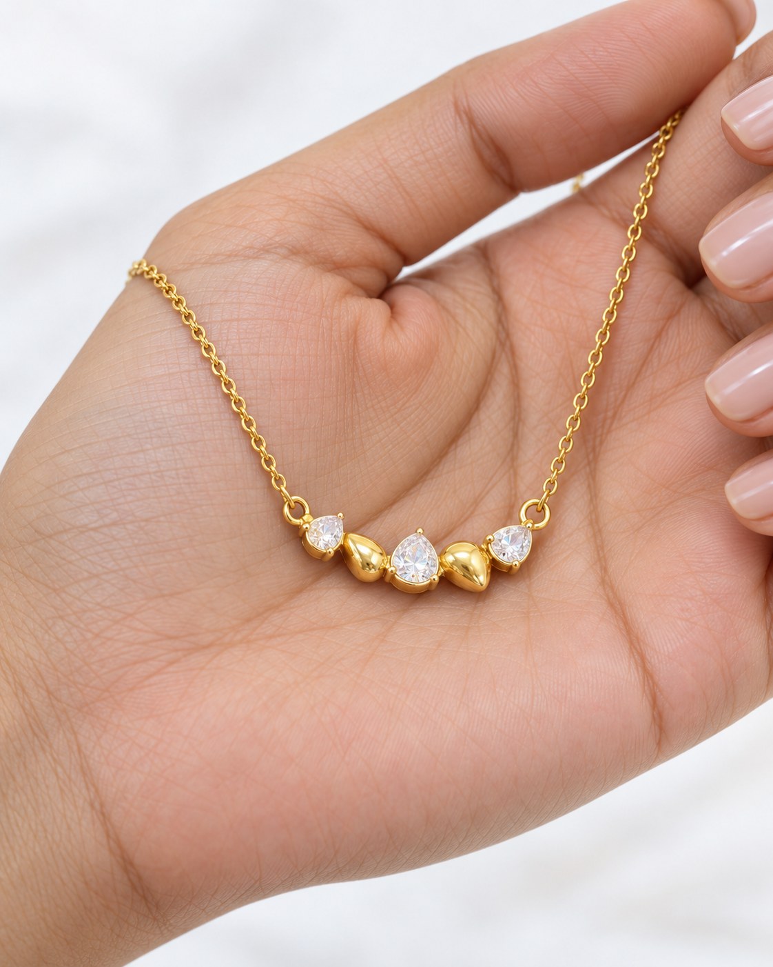 Paired Raven Drops Chain in white, pendant resting in the palm showing five clear and gold-tone drops