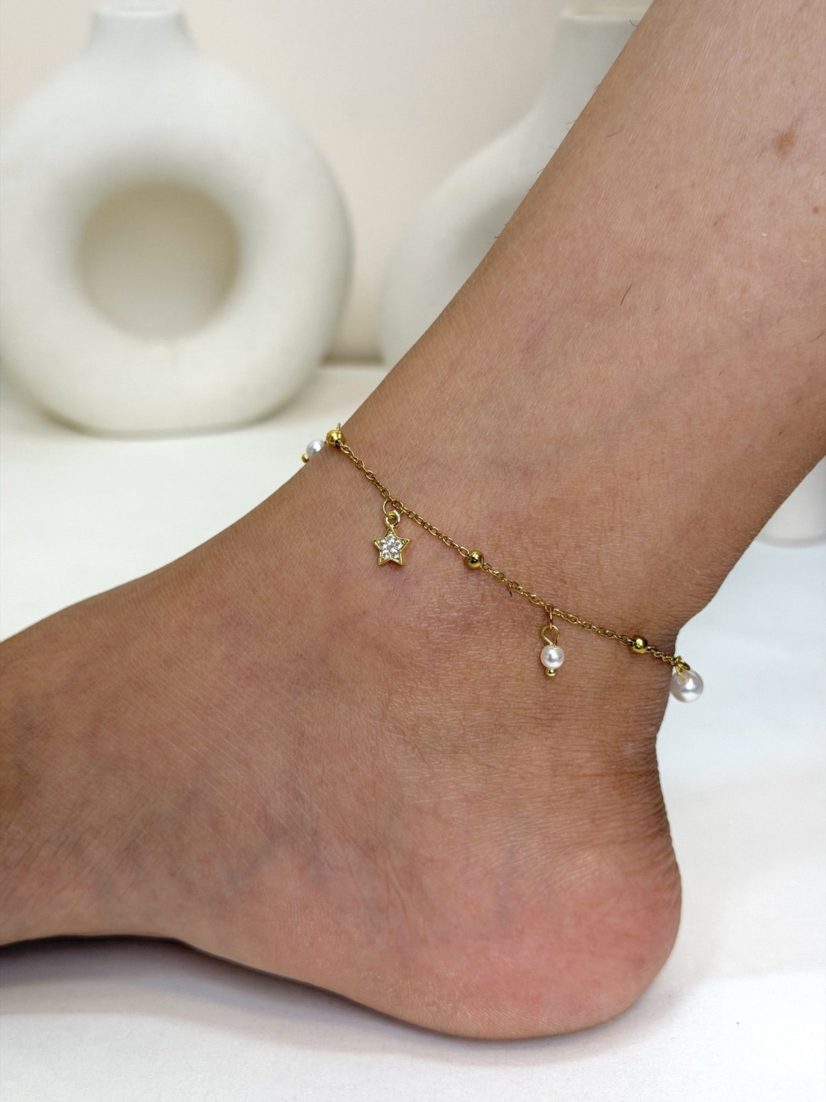 Paired Serelle Anklet in gold-tone, worn on the ankle with a clear-stone star charm and white bead drops