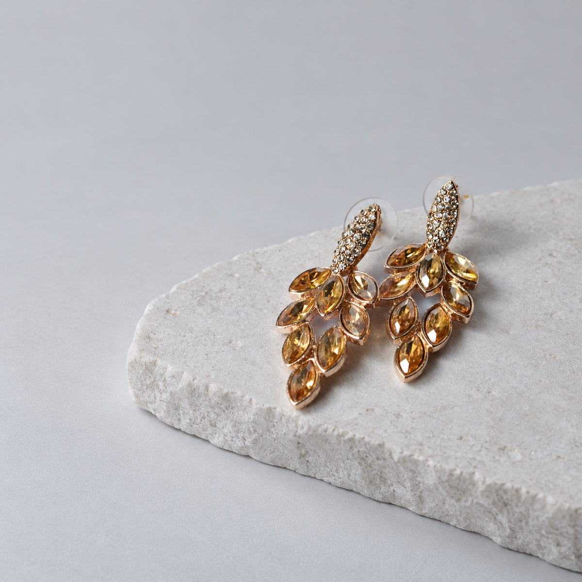 Paired Aurex Prestige gold leaf drop earrings with champagne stones on a stone plinth