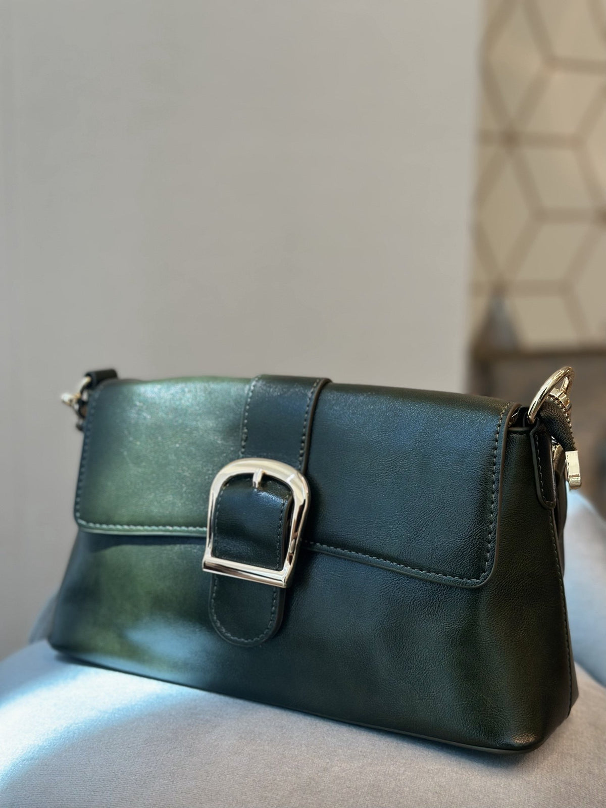 Paired Valora Buckle Sling Bag in deep green, seen from the side with a buckled flap and shoulder strap fittings