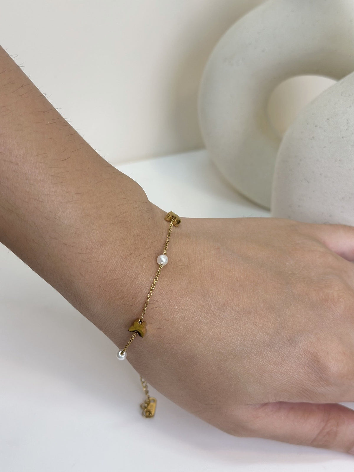 Paired Vianne Bracelet in gold-tone, close view on the wrist of the butterfly charms and white beads along the chain