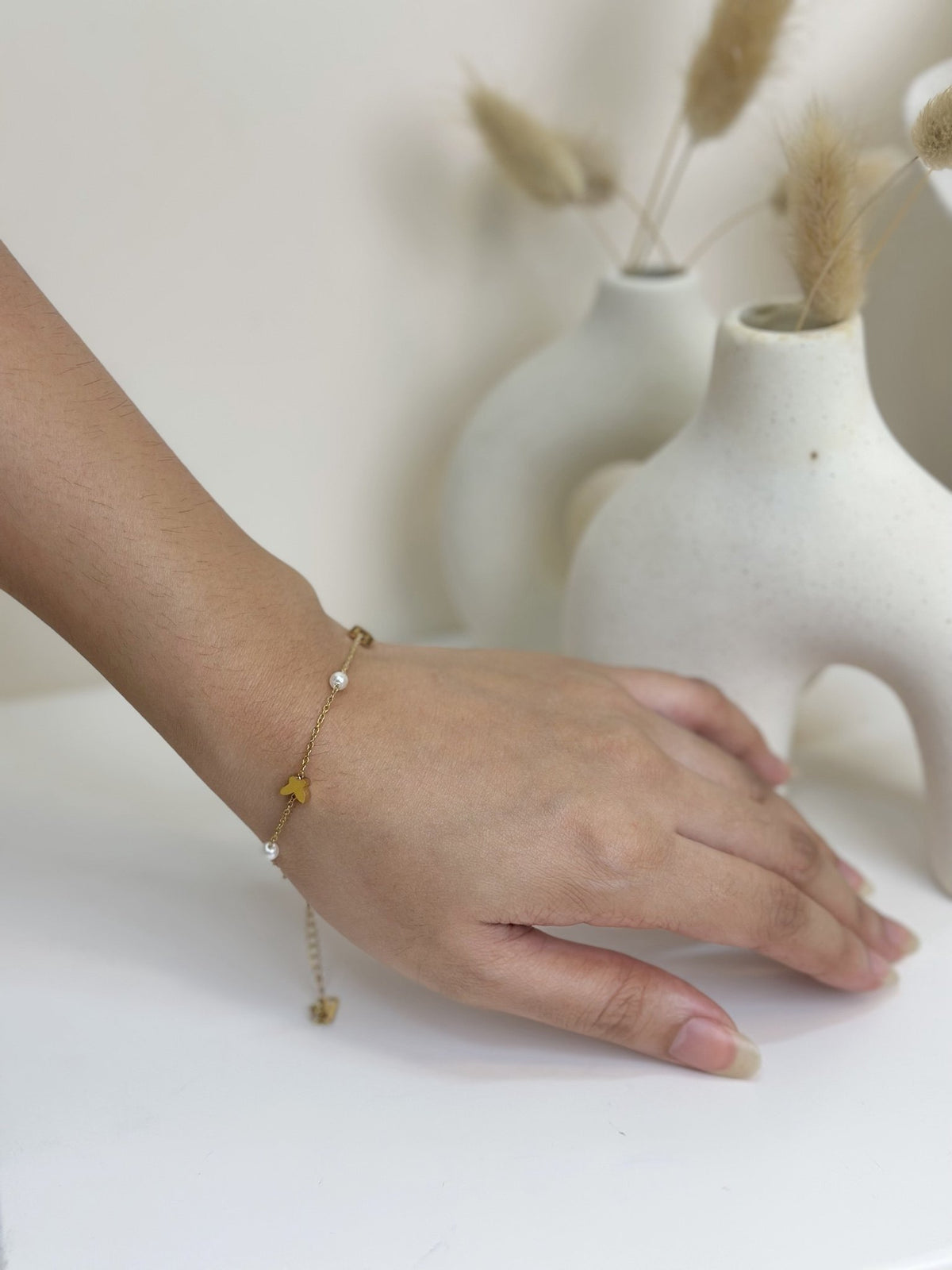 Paired Vianne Bracelet in gold-tone, worn on the wrist, with the adjustable tail and a small butterfly charm hanging