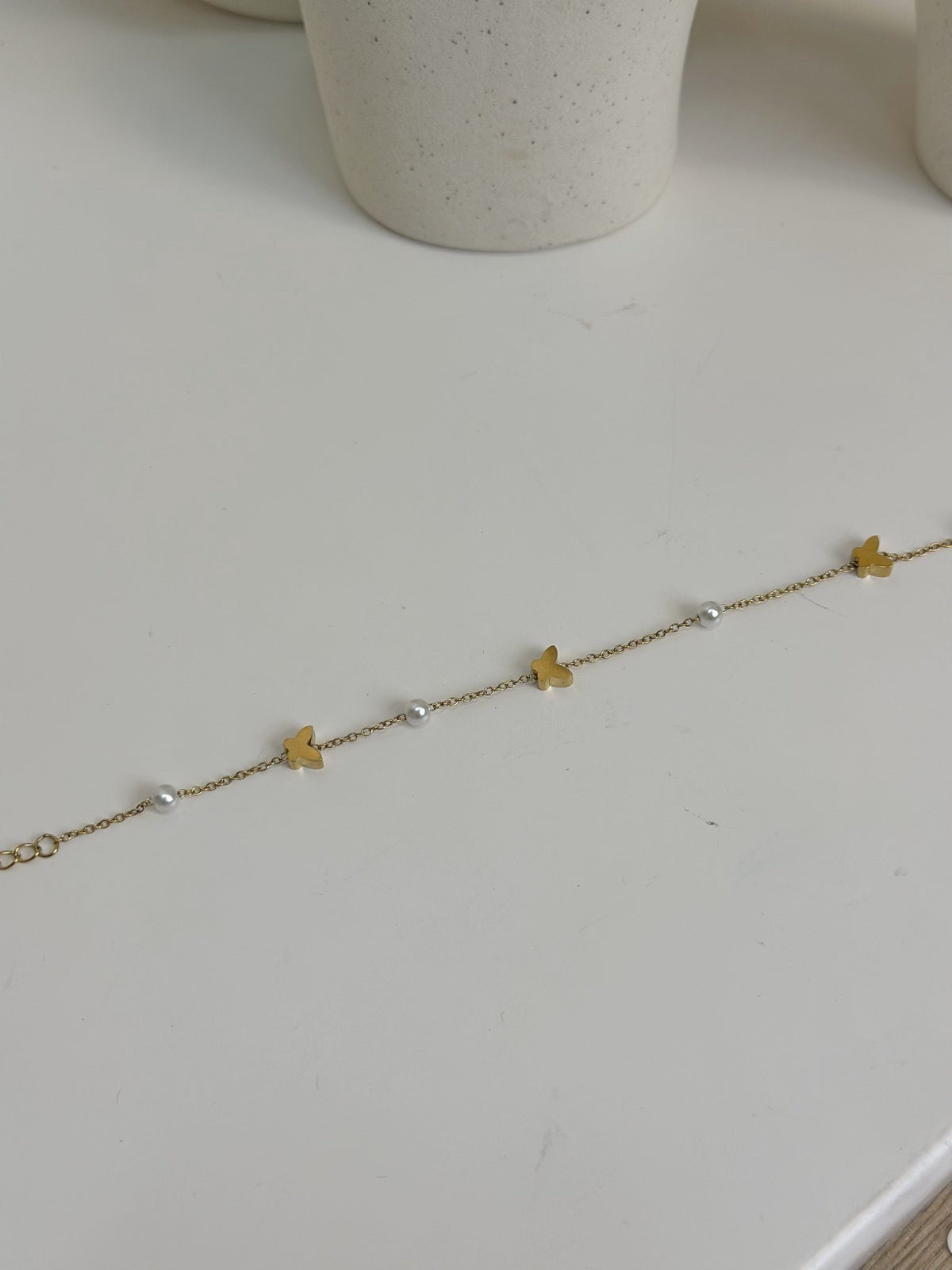 Paired Vianne Bracelet in gold-tone, laid flat to show the fine chain with butterfly charms and white beads alternating