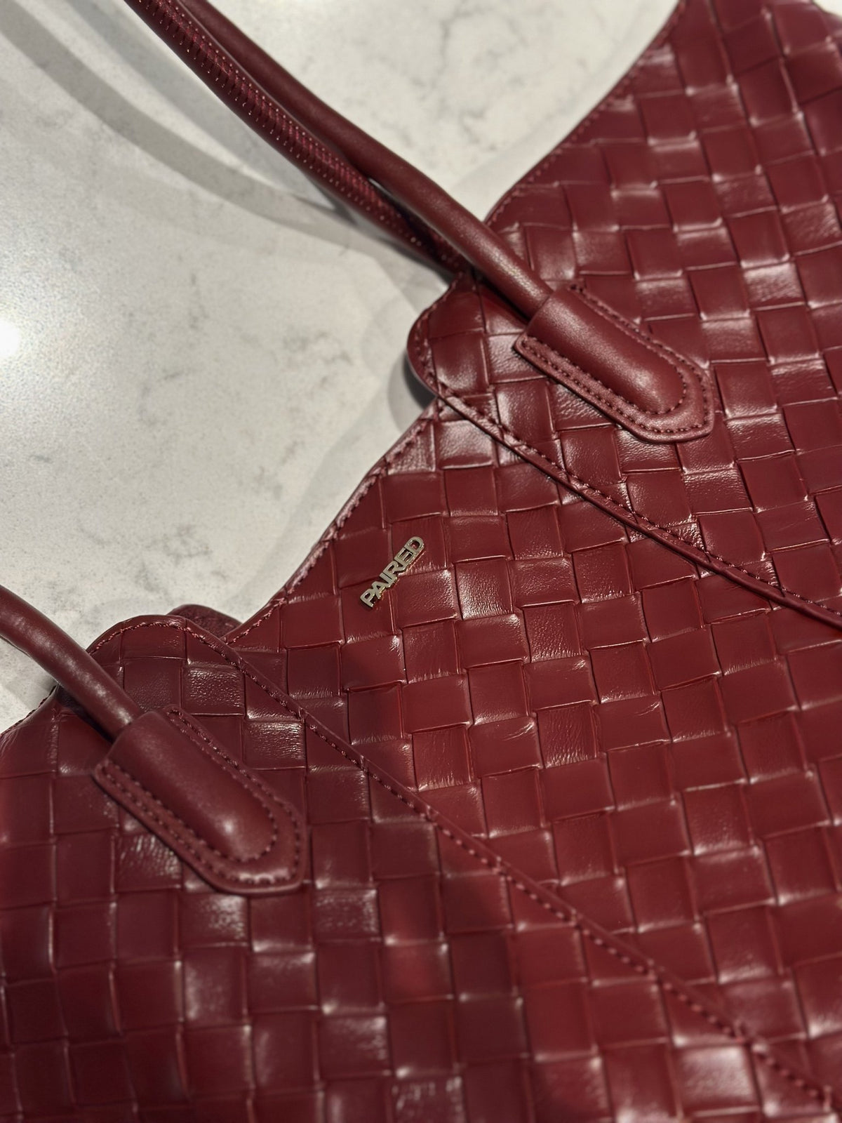 Paired Virelle Woven Bag in maroon, close-up of the woven texture, rolled handle and small logo plate