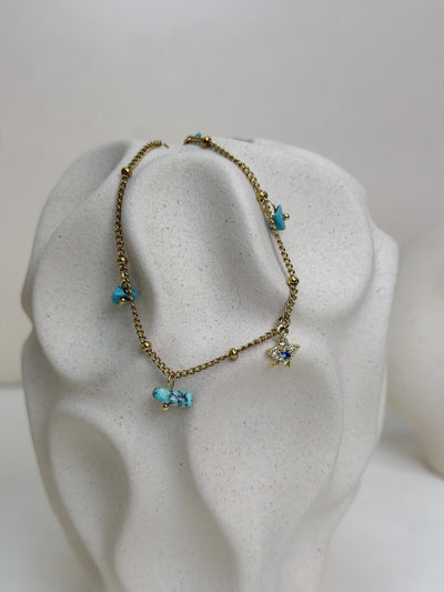 Paired Alvara Anklet in gold-tone, close view on a textured vase with turquoise-coloured stones and a star charm