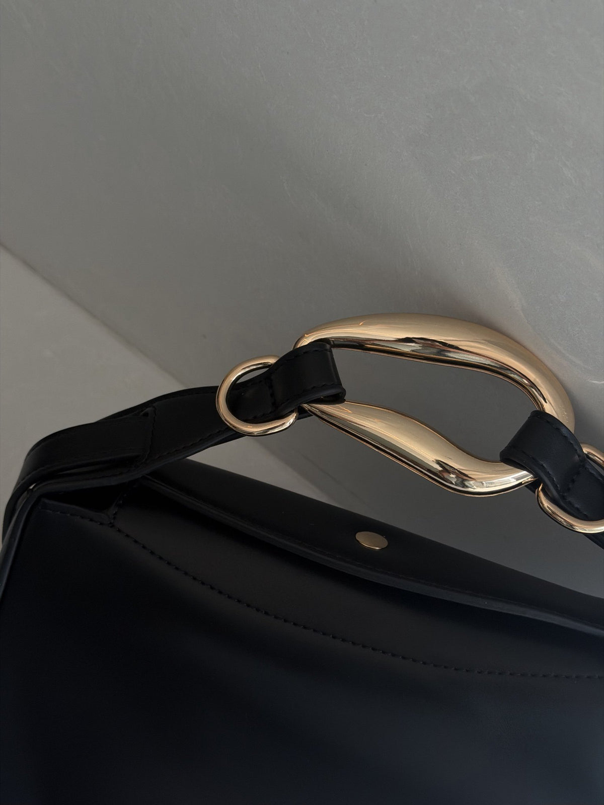 Paired Arden Soft Bag in black, close-up of the sculptural gold-tone ring handle and strap loops against the soft black body