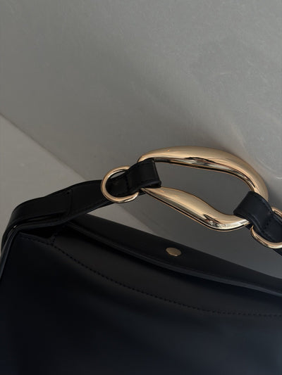 Paired Arden Soft Bag in black, close-up of the sculptural gold-tone ring handle and strap loops against the soft black body