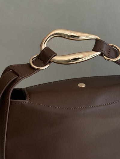 Paired Arden Soft Bag in coffee brown, close-up of the gold-tone ring handle, strap loops and snap detail on the back flap