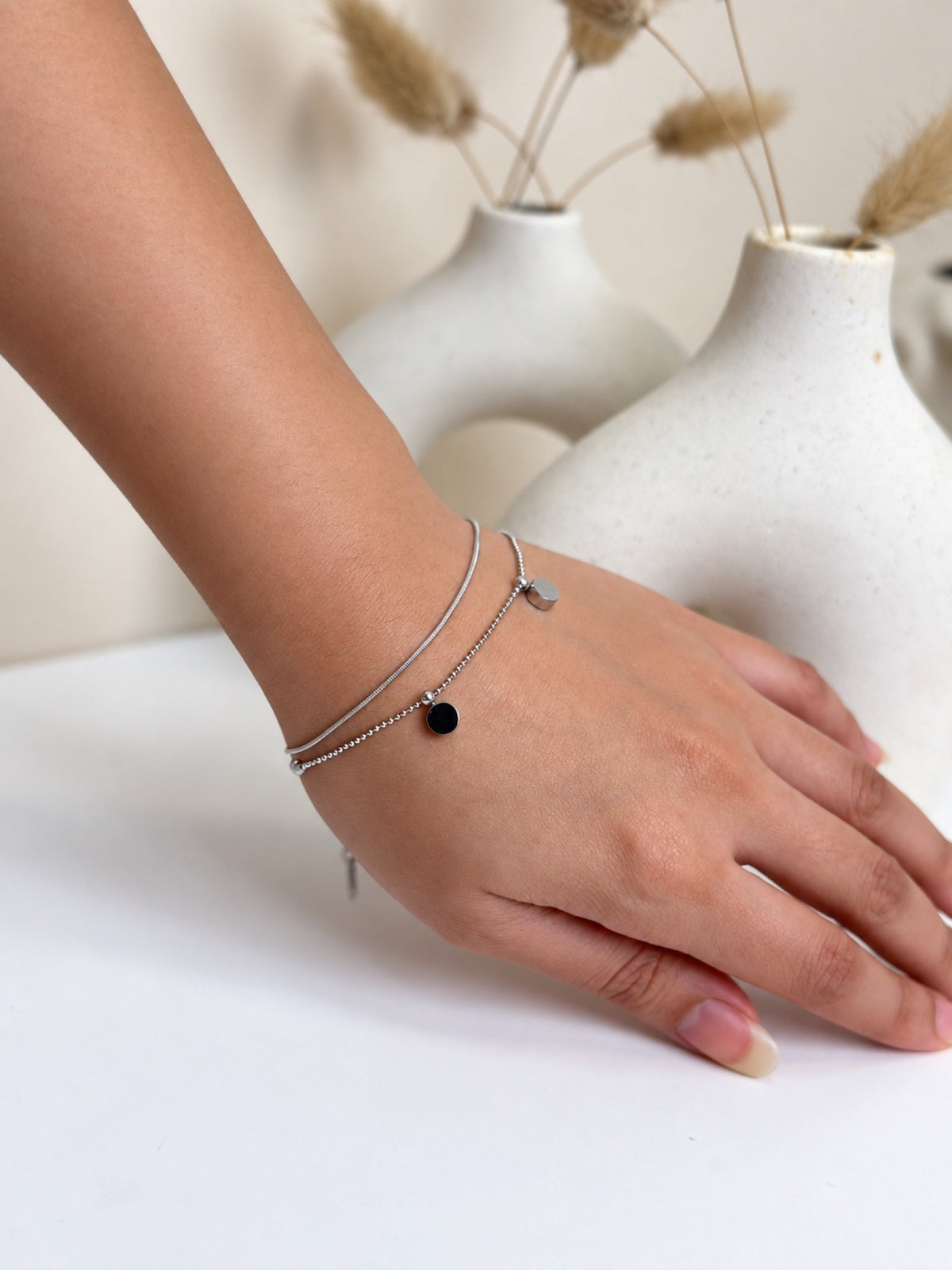 Paired Ariellea Bracelet in silver-tone, worn on the wrist with double strands and a dark round disc charm