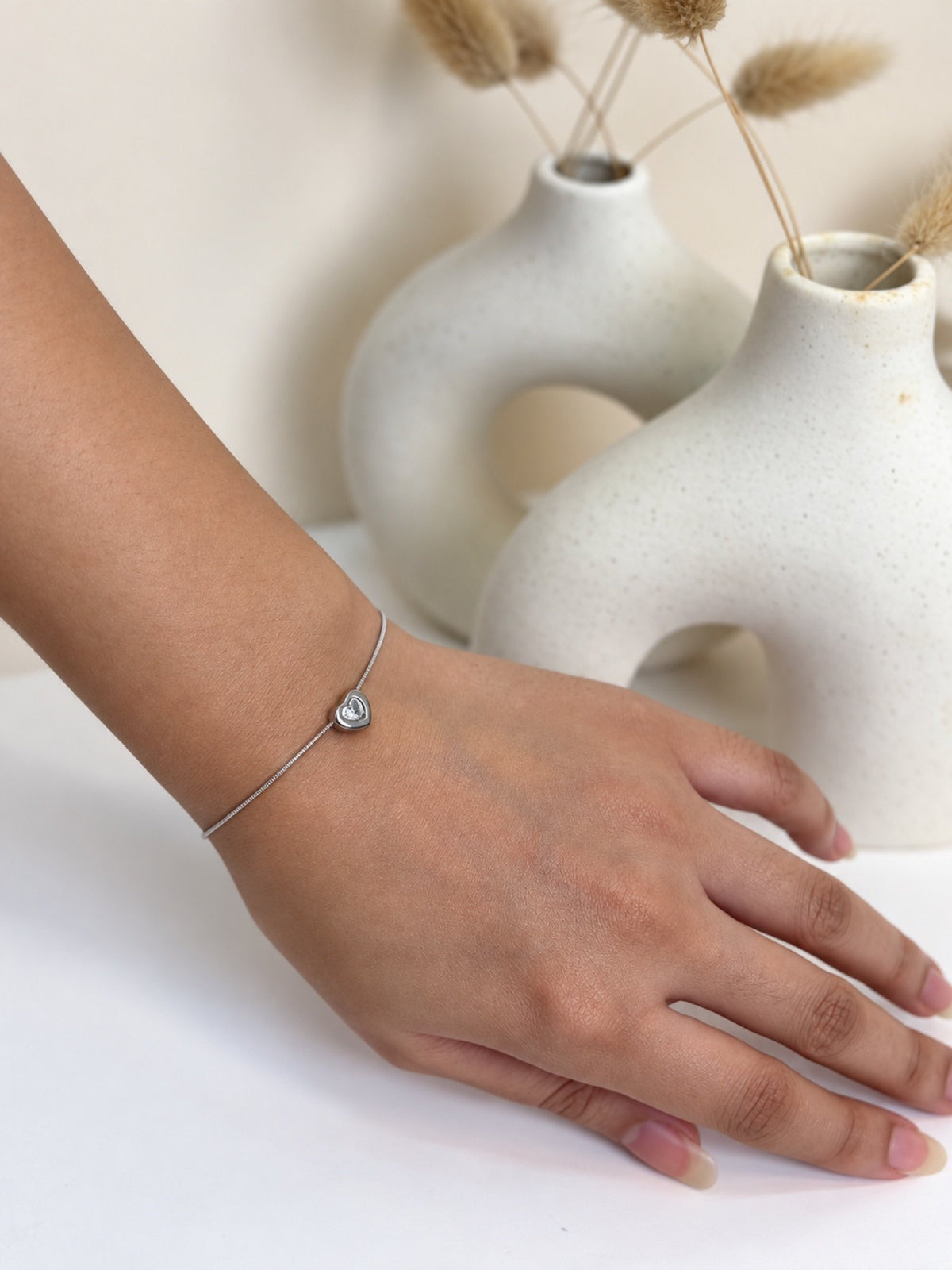 Paired Ariovelle Bracelet in silver-tone, worn on the wrist with a heart-shaped clear stone on a slim chain