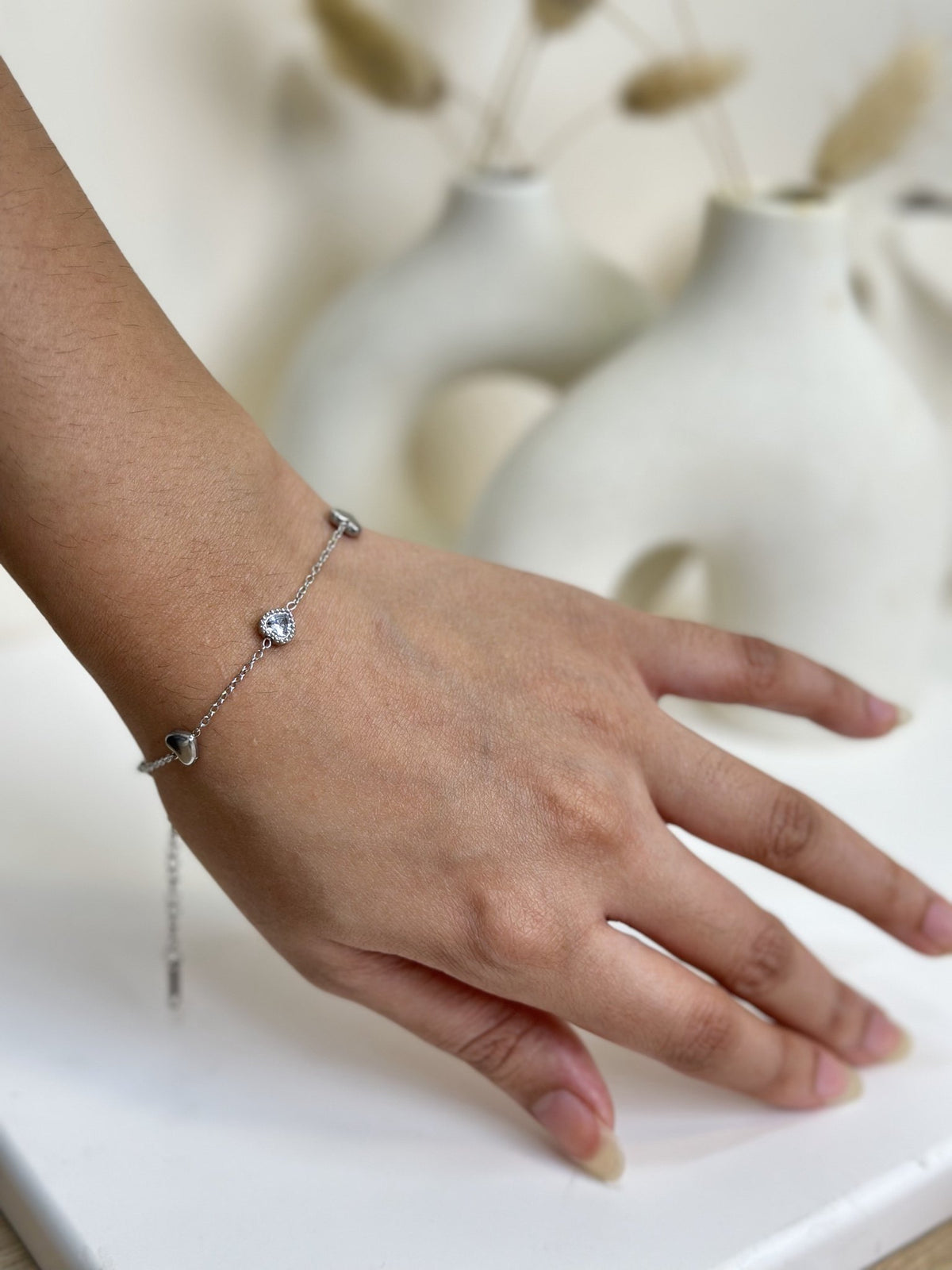 Paired Arlisse Bracelet in silver-tone, worn on the wrist with heart charms, a clear stone and extension chain