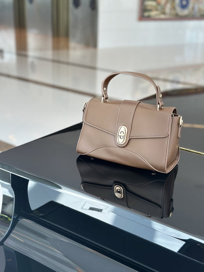 Paired Aurea Crest Bag in taupe apricot, with a top handle and gold-tone turn-lock, standing on a glossy black surface