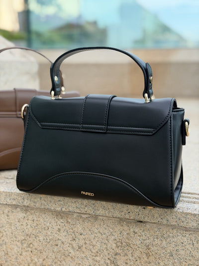 Paired Aurea Crest Bag in black, seen from the back with a top handle and stitched flap on a stone ledge