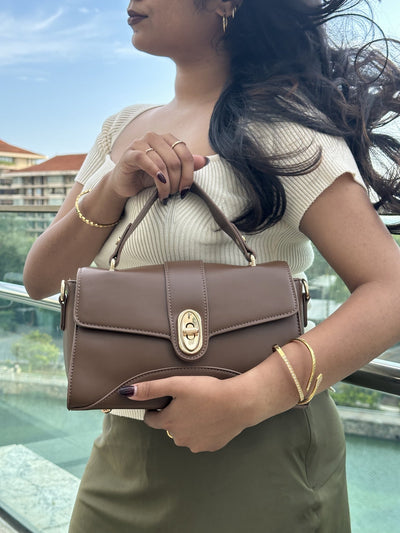 Paired Aurea Crest Bag in coffee brown, carried at the shoulder with a gold-tone turn-lock, photographed sideways