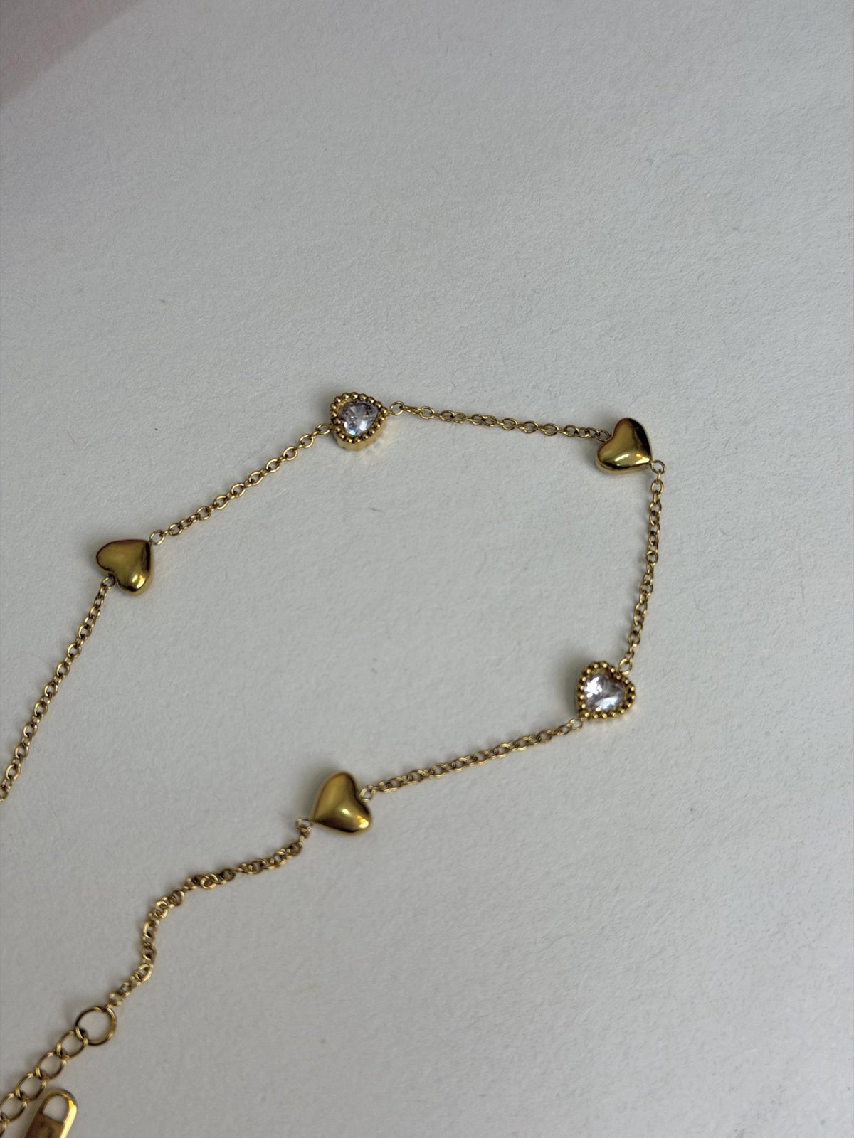 Paired Aurelia Anklet in gold-tone, laid flat showing the hearts, clear stones, fine chain and clasp end