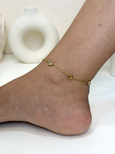 Paired Aurelia Anklet in gold-tone, worn on the ankle with small hearts and clear round stones on a fine chain