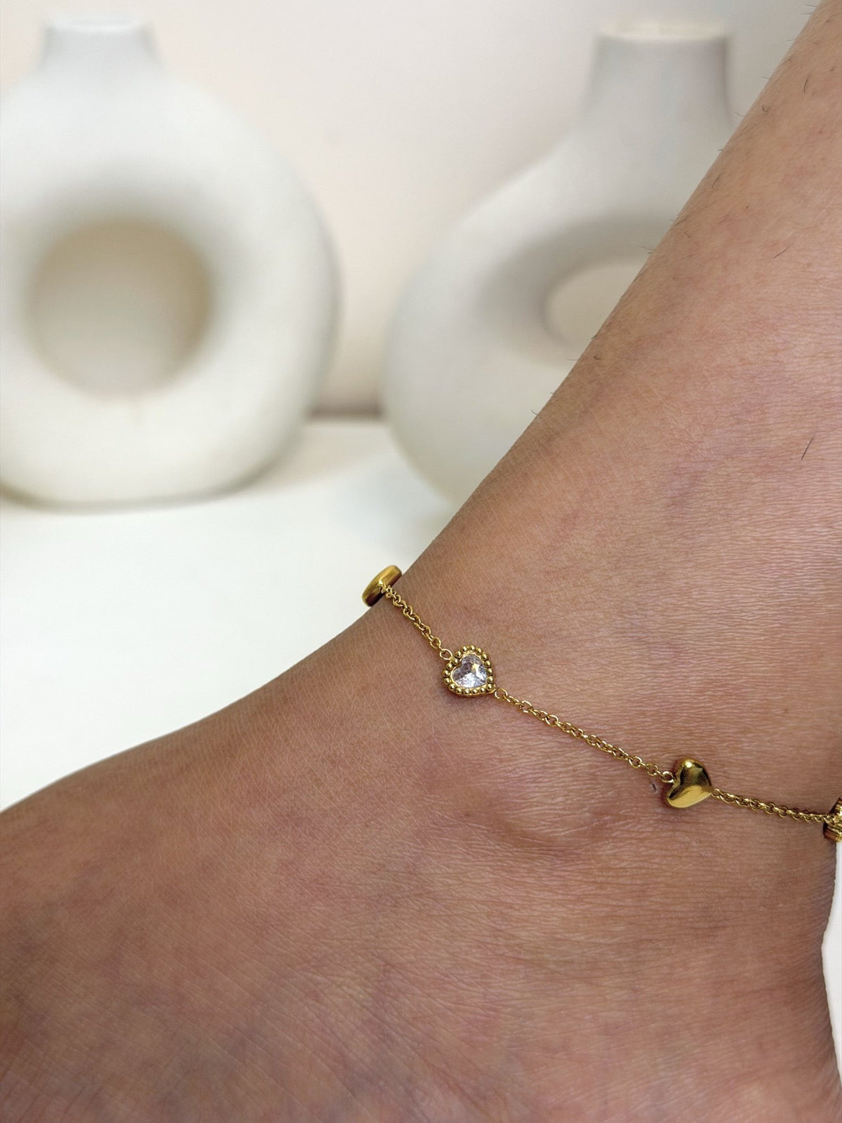 Paired Aurelia Anklet in gold-tone, close view on the ankle showing a clear round stone and a heart charm