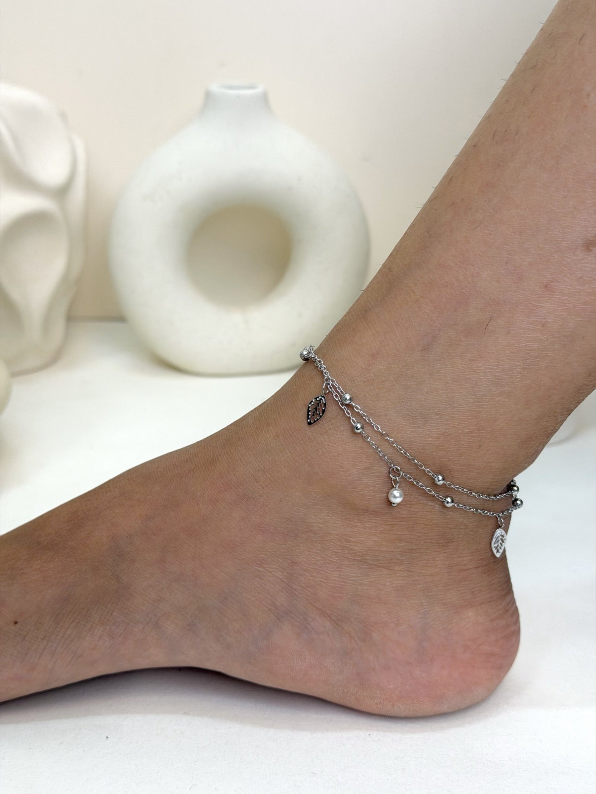 Paired Aurevia Anklet in silver-tone, side view on the ankle with layered chains, beads and a leaf charm