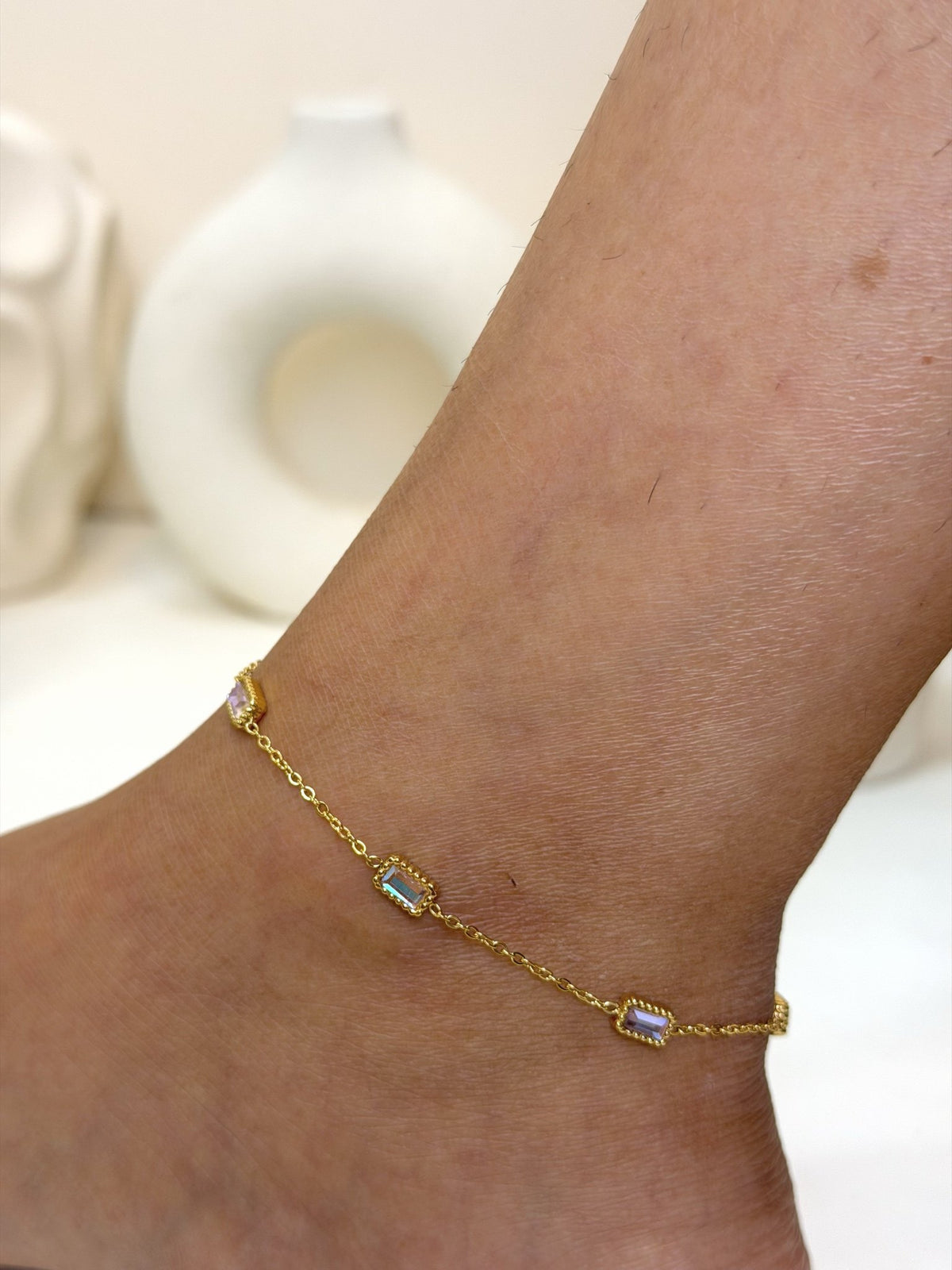 Paired Aveline Anklet in gold-tone, three-quarter view on the ankle with rectangular stones on a slim chain