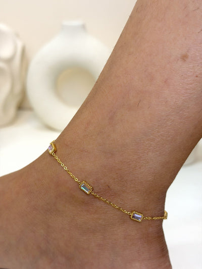 Paired Aveline Anklet in gold-tone, three-quarter view on the ankle with rectangular stones on a slim chain