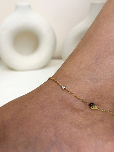 Paired Calisse Anklet in gold-tone, close view on the ankle showing a leaf-shaped charm and a tiny clear stone