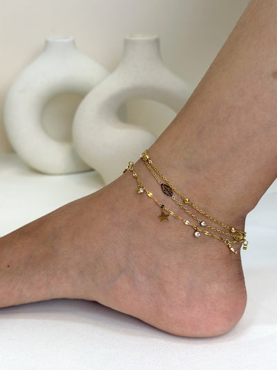 Paired Céliane Anklet in gold-tone, worn on the ankle with layered chains, beads, clear stones and small charms