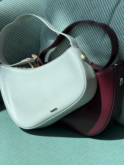 Paired Clarissa Chain Bag in white and burgundy lying together on a teal armchair, with straps and chain links
